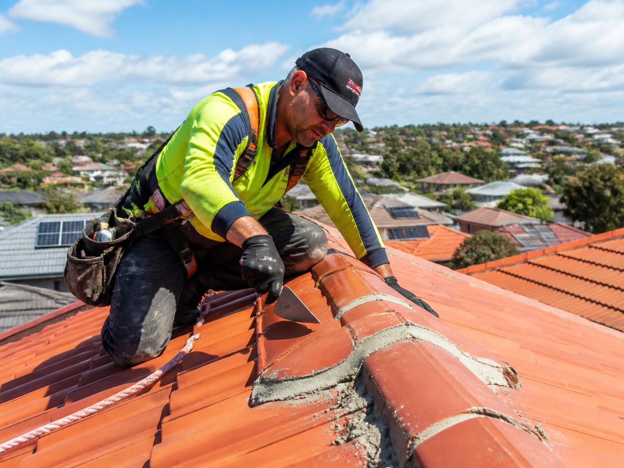 Roofer re-bedding ridge capping on a terracotta tile roof in Sydney