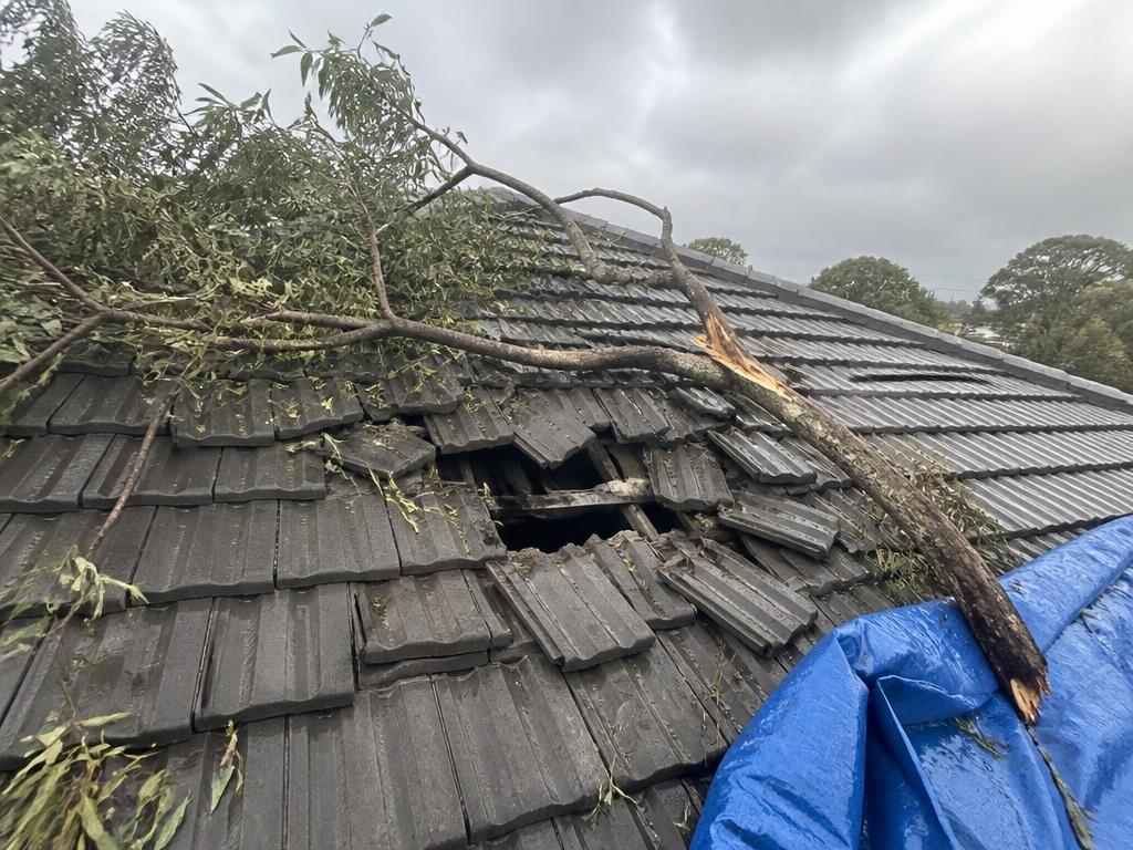 Charcoal concrete tile roof with broken tiles and fallen branch debris after a storm